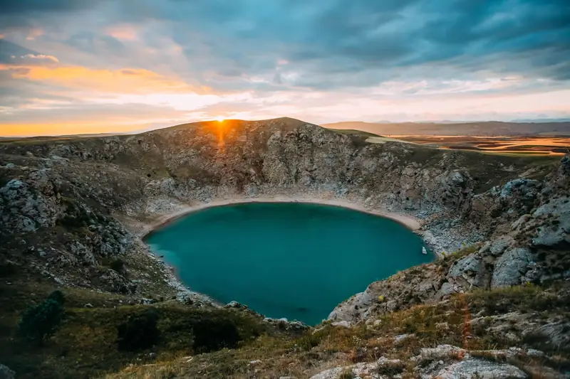 Turquoise lake inside a volcanic crater with the sun on the rim
